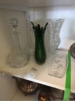 Overview of the glass lot with decanters, vases and tray on a white shelf