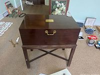 Full front view of wooden jewellery chest on decorative legs, visible brass handle and plate top