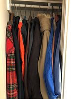 Closet view of men's jackets hanging, showing multiple jackets in various colors and styles including red plaid and winter coats