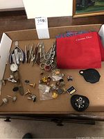 Wide shot of all items including Christian Dior scarf, wristwatch, cufflinks, pins, grooming tools, and outlet converter laid out on brown surface.
