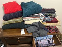 Full view of assorted wool sweaters, scarves, socks, nightwear, and other men's clothing items arranged on a wooden dresser and table.