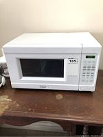 Front view of the small white microwave showing digital display, keypad, and door with window on a wooden surface.