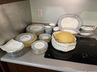 Full set arranged on kitchen counter showing stacks of plates, cups, saucers and cloth bag