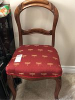 Front view of wooden chair showing burgundy upholstery with dragonfly pattern and visible carved wooden frame