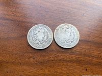 Two Venezuelan silver coins dated 1887 and 1888 on wooden surface.