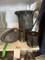 Image showing large silver plate jug with floral embossing, round bread platter with engraving, and two silver plate holders with cut-out patterns.
