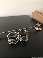 Photo of two sterling silver napkin rings and one sterling silver candle snuffer arranged on a black surface.