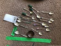 Top view of multiple sterling silver collectible spoons and one napkin ring arranged on carpet