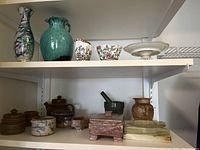 Two marble ashtrays, granite mortar and pestle, granite jewelry box, decorative pottery bowls, Coalport China sugar bowl and creamer on shelves.