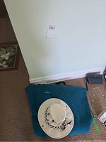 Cream Tilley hat on folded teal L.L. Bean fleece blanket near wall corner on carpet