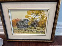 Framed oil painting of a rural scene with a barn, large yellow-leafed tree, and fence, signed Trudy Doyle.