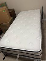 Full view of twin bed setup including pillow top mattress on box spring with metal frame and lift assist visible.
