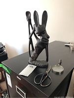 Photo showing the wooden abstract statue alongside the sewing scissors and magnifying glass on a black surface.