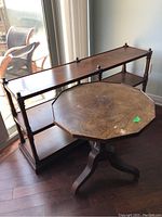 Wooden shelf with metal finials and octagonal parquet side table positioned beside a window on hardwood floor.