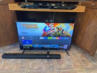 42-inch Insignia Fire TV turned on displaying Dungeons & Dragons streaming content, with sound bar and woofer in foreground and remote on sound bar.