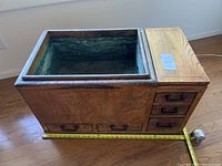 Photo showing the top and front view of the antique wooden hibachi, copper lined interior and drawers, along with a tape measure to indicate size.