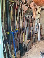 Overall view of assorted gardening tools hanging on a wall including shovels, rakes and hoes.