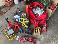 Full lot showing floor jacks, jack stands, battery chargers, flood light, clip-on wheel studs in red bag, and chains