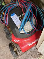 Red Homelite electric lawnmower with 12 amp motor label, power cord on top, and front wheel visible.