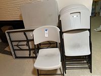 Six beige Lifetime plastic folding chairs stacked and arranged next to two folding tables with plastic tops, showing items in the lot.