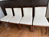 Four dining chairs with white textured upholstery and wooden frames, displayed side by side.