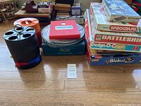 Photo showing various vintage board games stacked together with a rotating plastic carousel game piece stand and a boxed Hangman game.