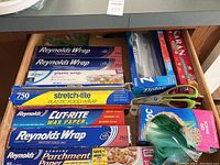 Photo of entire drawer with various kitchen wraps, papers, bags and scissors.