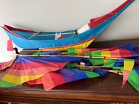 Side view of the boat shaped kite with colorful rainbow sails folded next to it on a wooden surface.