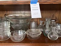 Photo of various clear glass bowls, pitchers, and serving pieces on wooden shelf.