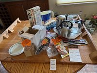 Photo of assorted kitchen items including kettles, grinder, slicer, and utensils on round wooden table