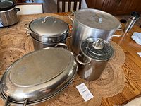 Overview of assorted stainless steel cooking pots and roasting pan with lids on a wooden table