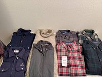 Full view of six wool shirts and sweaters arranged on floor showing variety of colors and styles