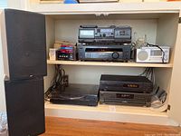 Wide view of the stereo equipment set inside a shelf including the speakers, turntable, and various audio components stacked on shelves.