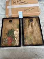 Both Takimoma art doors side by side with original shipping box in background showing 'Fragile' marking, floral gold-leaf style designs under glass in black wood frames, one door shows more prominent flower cluster.