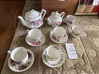 Overall lot showing two porcelain teapots, six teacups and four saucers arranged on beige carpet.