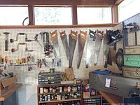 Photo of pegboard with seven hand saws hanging and various hand tools such as pliers and files hanging and small hardware below.