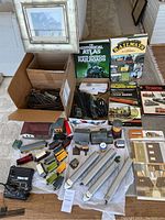 Photo showing model train cars, various tracks in boxes, transformers, and railroad books spread out on floor