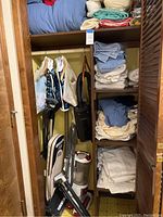 Closet interior showing two Oreck upright vacuums, one Shark vacuum on the floor, shelves with folded towels and blankets in blue, beige, cream colors.