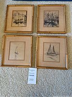 Four bamboo framed art prints depicting sailboats in black and white on beige matting, arranged on carpeted floor.
