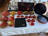 Overview of vintage plastic Asian dinnerware collection arranged on table with various matched sets in red, gold, and black showing plates, bowls, small cups with saucers and trays