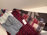 Photo showing two wool throws, a grey ribbed knit turtleneck sweater, a blue sweater, and a red and blue Pendleton tartan plaid skirt.