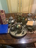 Full view of all silver plated dinnerware and silverware on a table including teapots, pitchers, tray, goblets, sugar bowl and creamer, and decorative horse figurine.