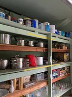 Shelves filled with various pots and pans, including large stockpots, saucepans, and a colander, as well as some household containers on top shelf.