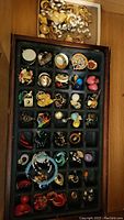 Various costume jewelry pieces arranged in black tray showing rings, earrings, clip-ons, and necklaces with colorful and gold-tone designs.