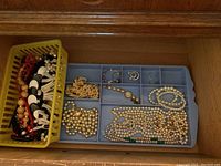Drawer with plastic bins holding assorted costume jewelry including faux pearl necklaces and other beaded jewelry.