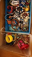 Top view of blue tray containing various bracelets and necklaces with mixed colors and materials including beads and plastic bangles.
