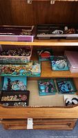 Full view of drawers and trays containing assorted costume jewelry and watches, including bracelets, rings, chains in gold and silver tones.