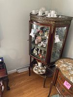 Front three-quarter view of the cabinet showing marble top, brass gallery rail and interior shelves