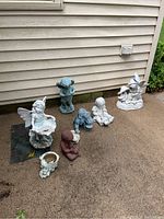 Photo showing all seven statues placed on concrete near siding; includes fairies, children, and dog statues