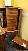 Exterior of wood jewelry armoire with multiple drawers, lockable side door open with hooks for necklaces